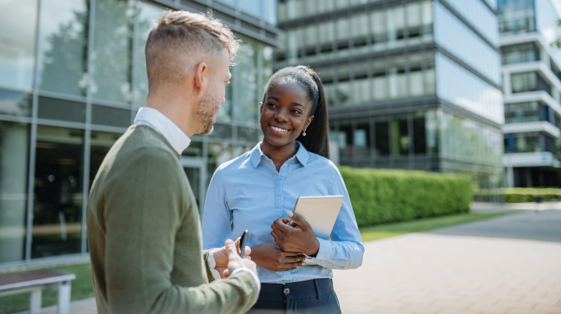 Two professionals stand in a courtyard talking and smiling