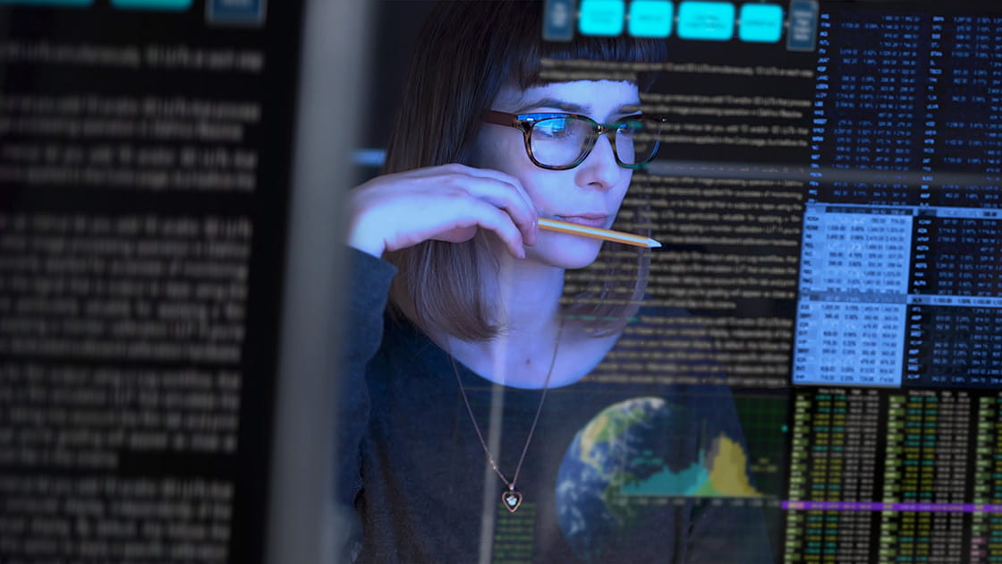 Woman looking intently at data on transparent computer screen;  she is white, 30s, wearing glasses and has a bob haircut with a blunt full fringe 