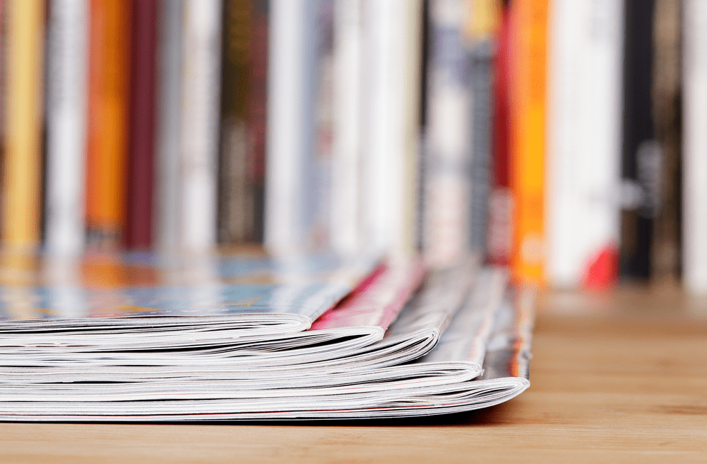 four magazines stacked on a table in front of a bookshelf