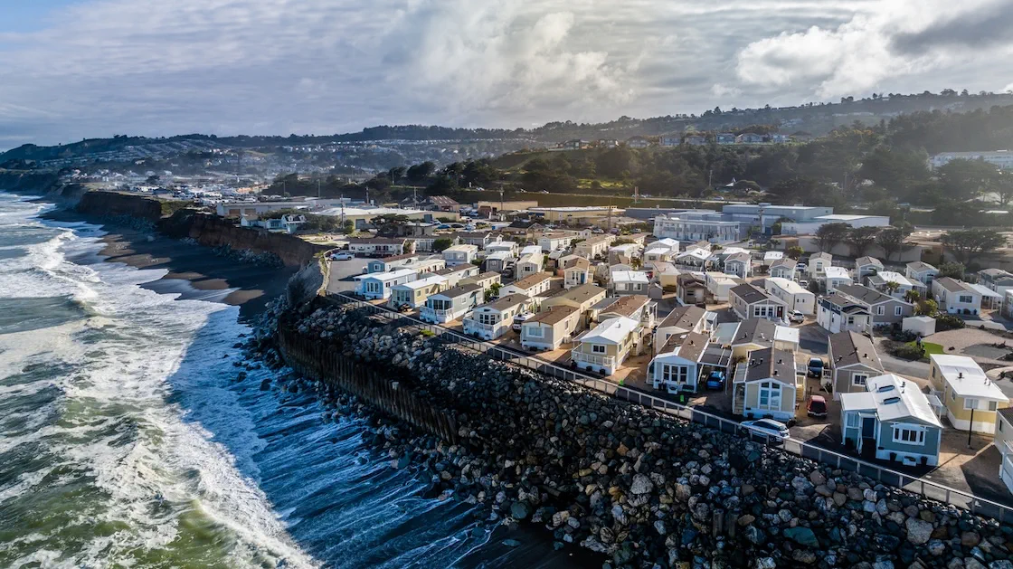 Aerial view of coastal homes on top of rocky cliffs, overlooking waves crashing on a beach.