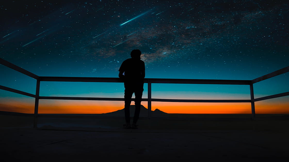 Silhouette of person looking up at meteor shower in night sky