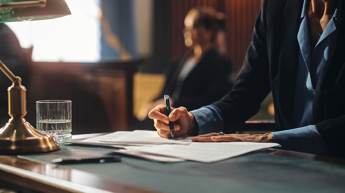 Close-up of female solicitor / advocate's hands, taking notes during trial / hearing, on the desk there are papers, an old fashioned-green shaded lamp and a glass of water