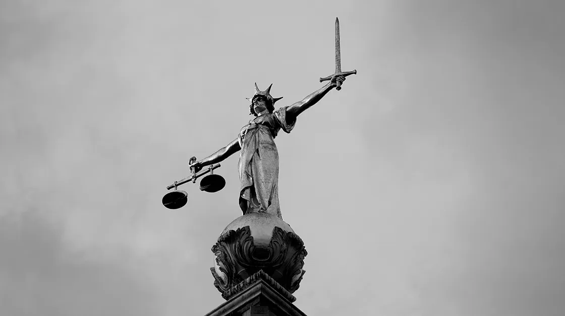 A statue of Lady Justice stands atop the Old Bailey in London on an overcast day.