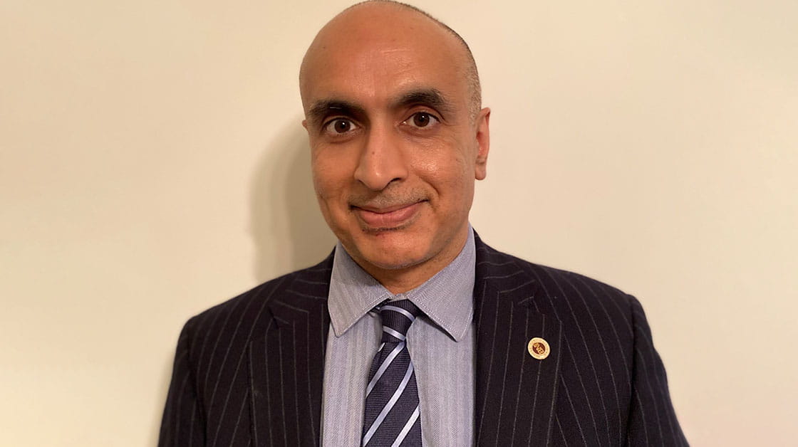 Sundeep Bhatia is a man of Indian heritage with closely cropped grey hair. He is smiling and wears a dark pinstriped suit, pale grey shirt and navy striped tie.