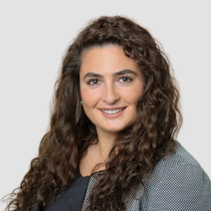 Victoria Teymourian-Yates is a woman with curly hair, wearing a grey jacket and smiling at the camera