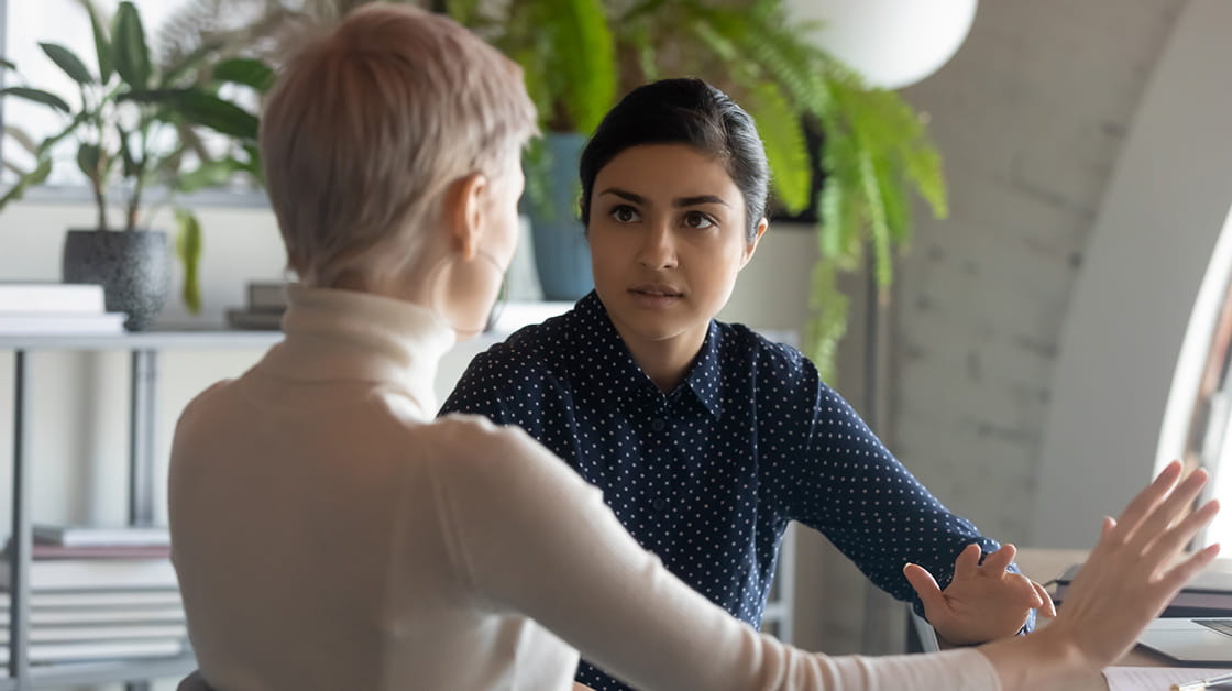 A woman with dark hair has a tense conversation with another woman.