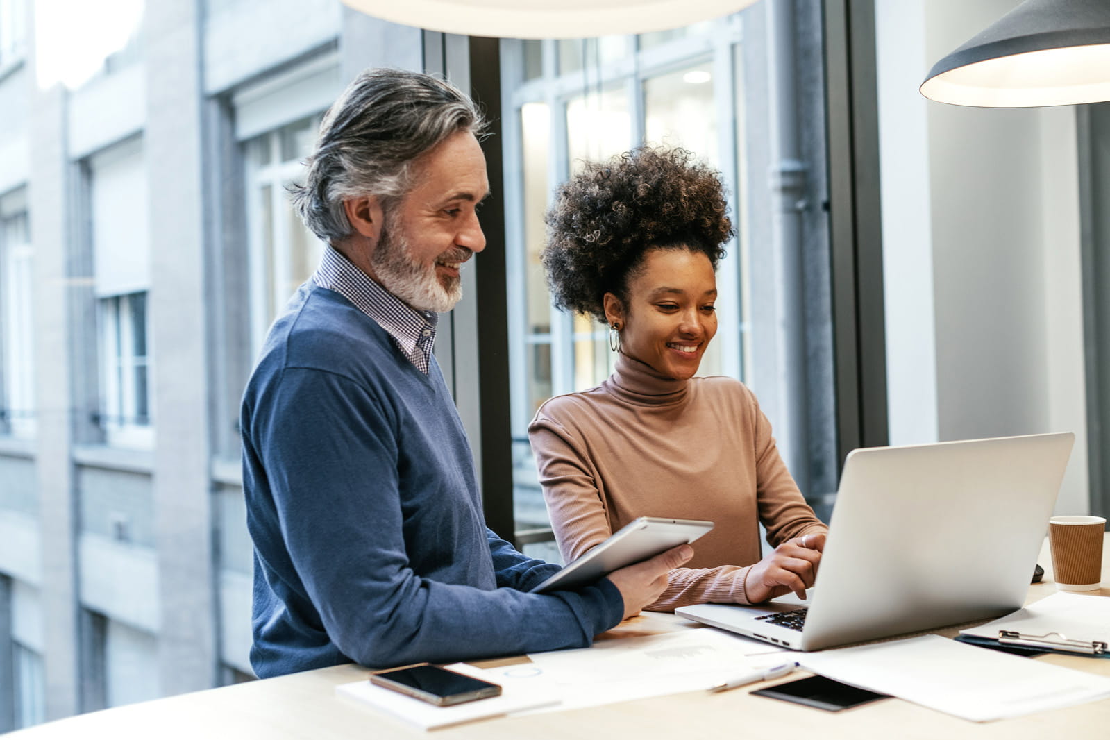 An older man shows a younger woman something on a laptop in an office