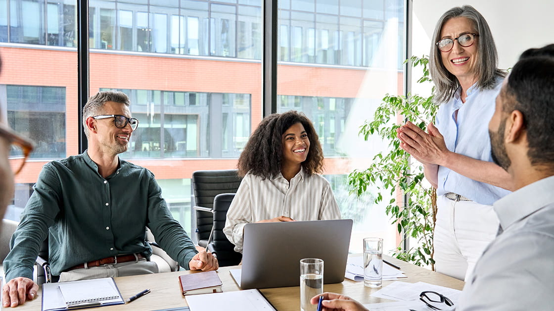 A diverse group of colleagues sits around a desk in a meeting room having a lively discussion