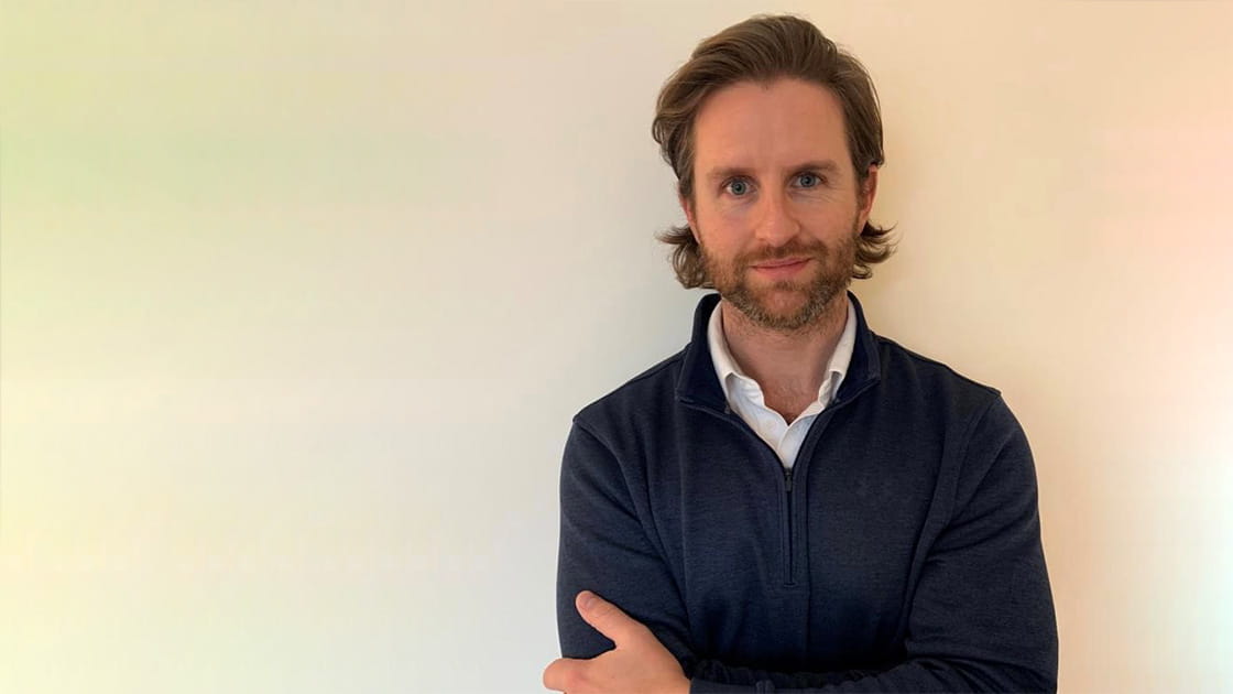 Tom Stenner-Evans is a white man, with chin-length brown hair and a trimmed beard. He's wearing a white shirt under a blue fleece.