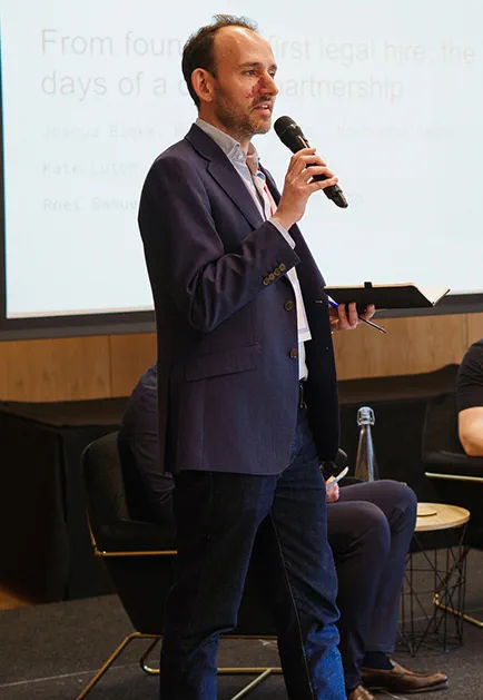 A man gives a talk and gestures in a room full of people 