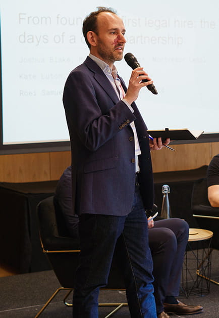 A man gives a talk and gestures in a room full of people 