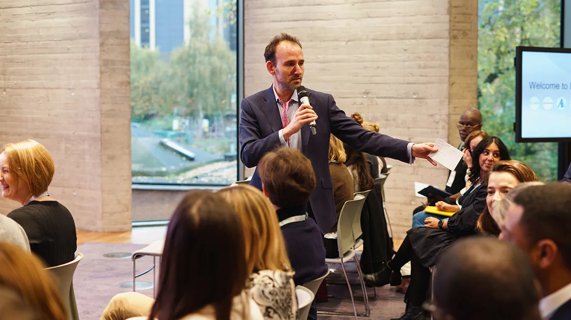 A man gives a talk and gestures in a room full of people