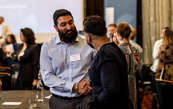 Two in-house solicitors shake hands at a networking event.