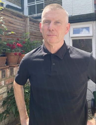 Solicitor Joe Kelly stands in a garden wearing a smart black polo shirt