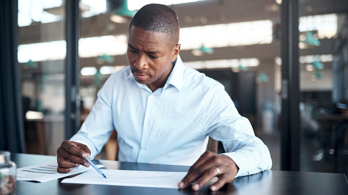  A man in a blue shirt sits at a desk and looks over a document.