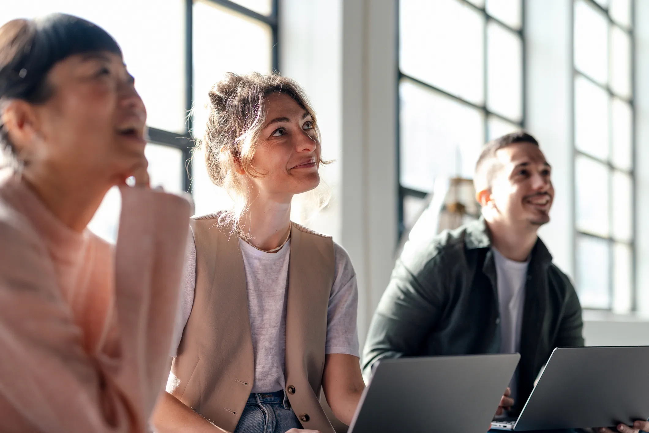 Three people listening to someone and smiling.