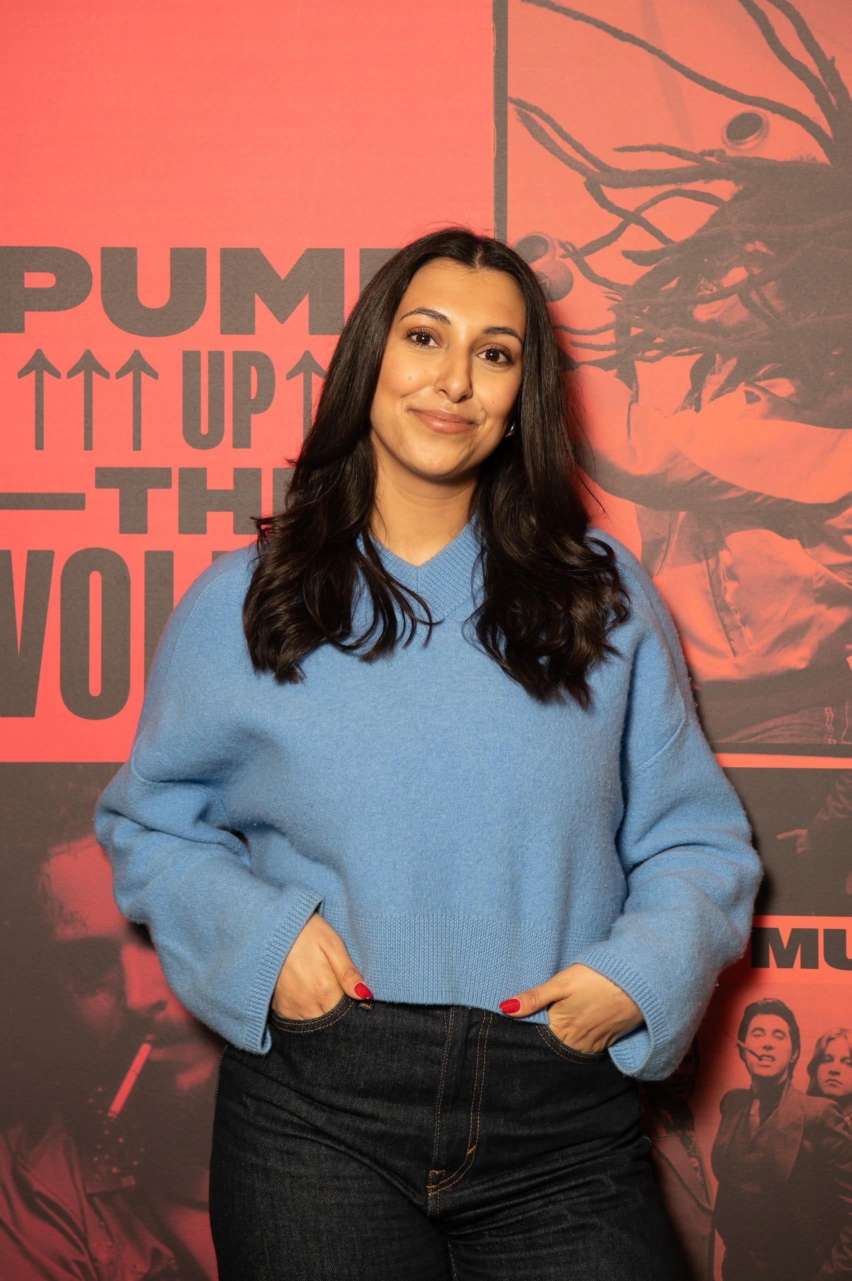 Talia Shabatai stands in front of an orange background.