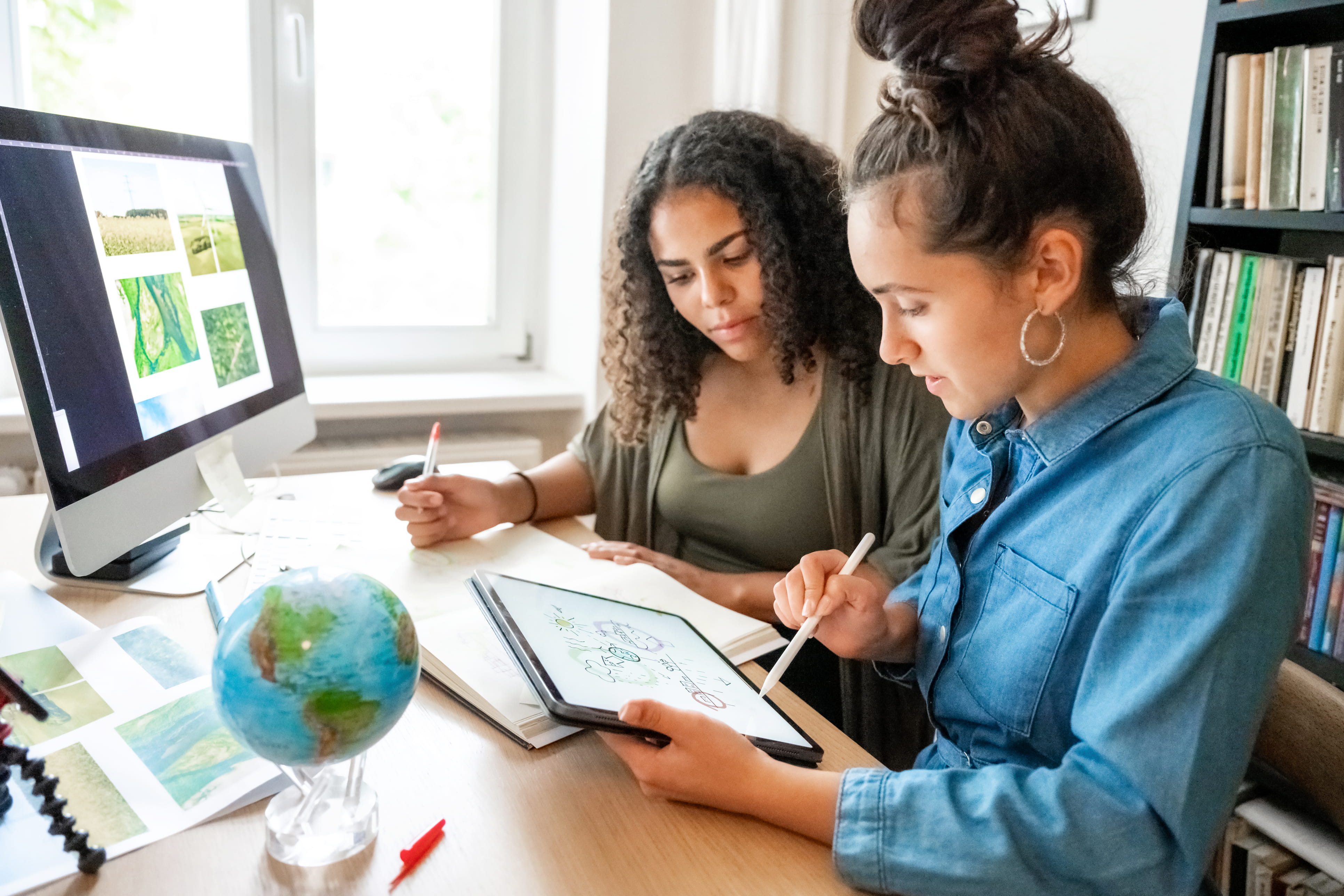 Two women look at the screen with climate related images and a globe on the desk 