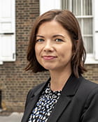 Tríona Lenihan is a white woman with short brown hair. She is standing outside wearing a dark patterned blouse and a black jacket. She is smiling with her mouth closed.
