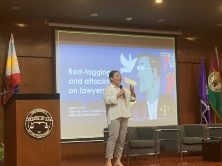 Human rights lawyer Kristina Conti delivers a presentation. She is wearing a white shirt and holding a microphone