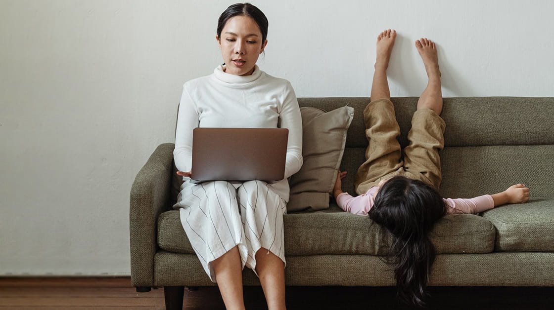 Mother with laptop sitting next to little girl laying on sofa