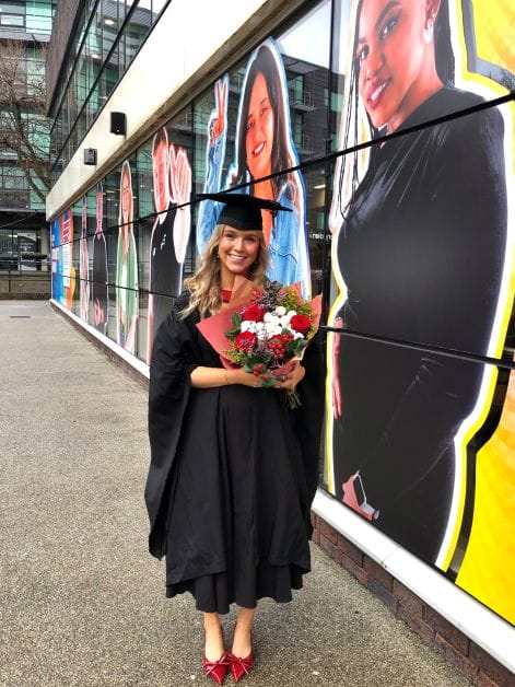 A woman in a graduation gown holds a bunch of flowers.