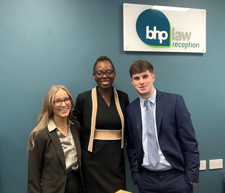 Three people in office wear smile at the camera.