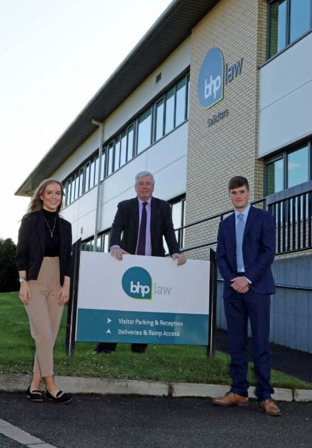 A woman and two men stand outside a law firm