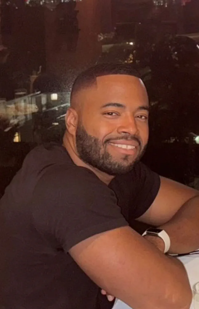 Jivaan Bennett smiles at the camera in front of a city skyline.