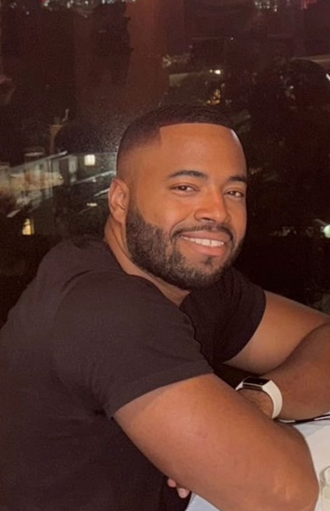 Jivaan Bennett smiles at the camera in front of a city skyline.