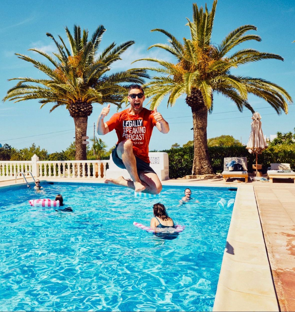 Robert Hanna jumps into a pool, with palm trees in the background.