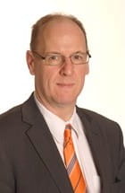 A man wearing glasses and a suit smiles