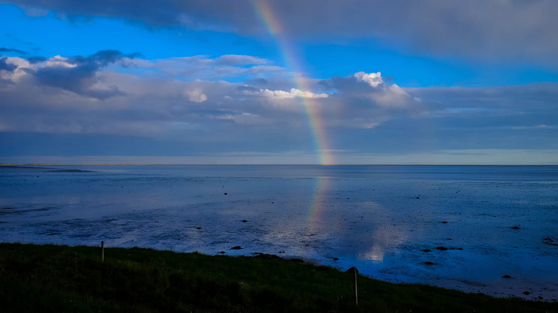 Rainbow over beach at low tide, blue sky and clouds reflected on the shallow water
