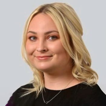 Demi Rixon is a white woman with shoulder-length blonde wavy hair. She is smiling and wears a black dress and gold necklace.