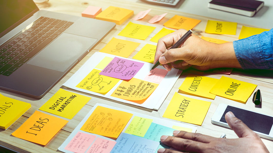A person writes business strategy and marketing ideas on sticky notes