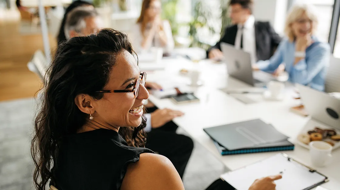 Smiling woman sits at meeting table with colleagues