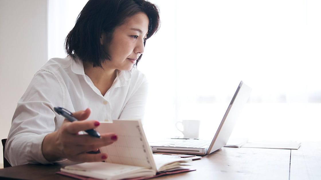 Woman managing finances using laptop and writing in notebook