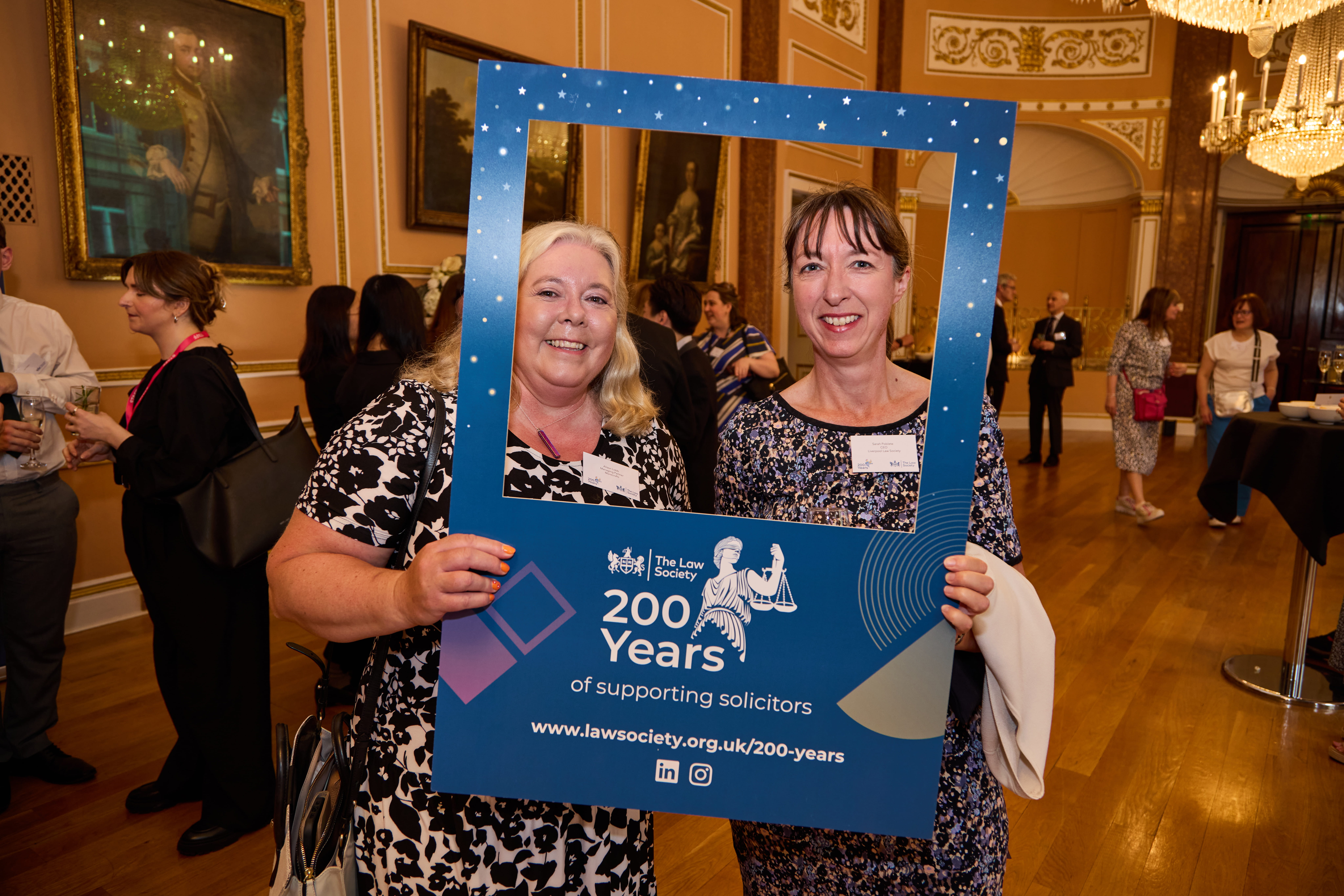 Two women, one blonde, one brunette posing and smiling behind bicentenary photo frame