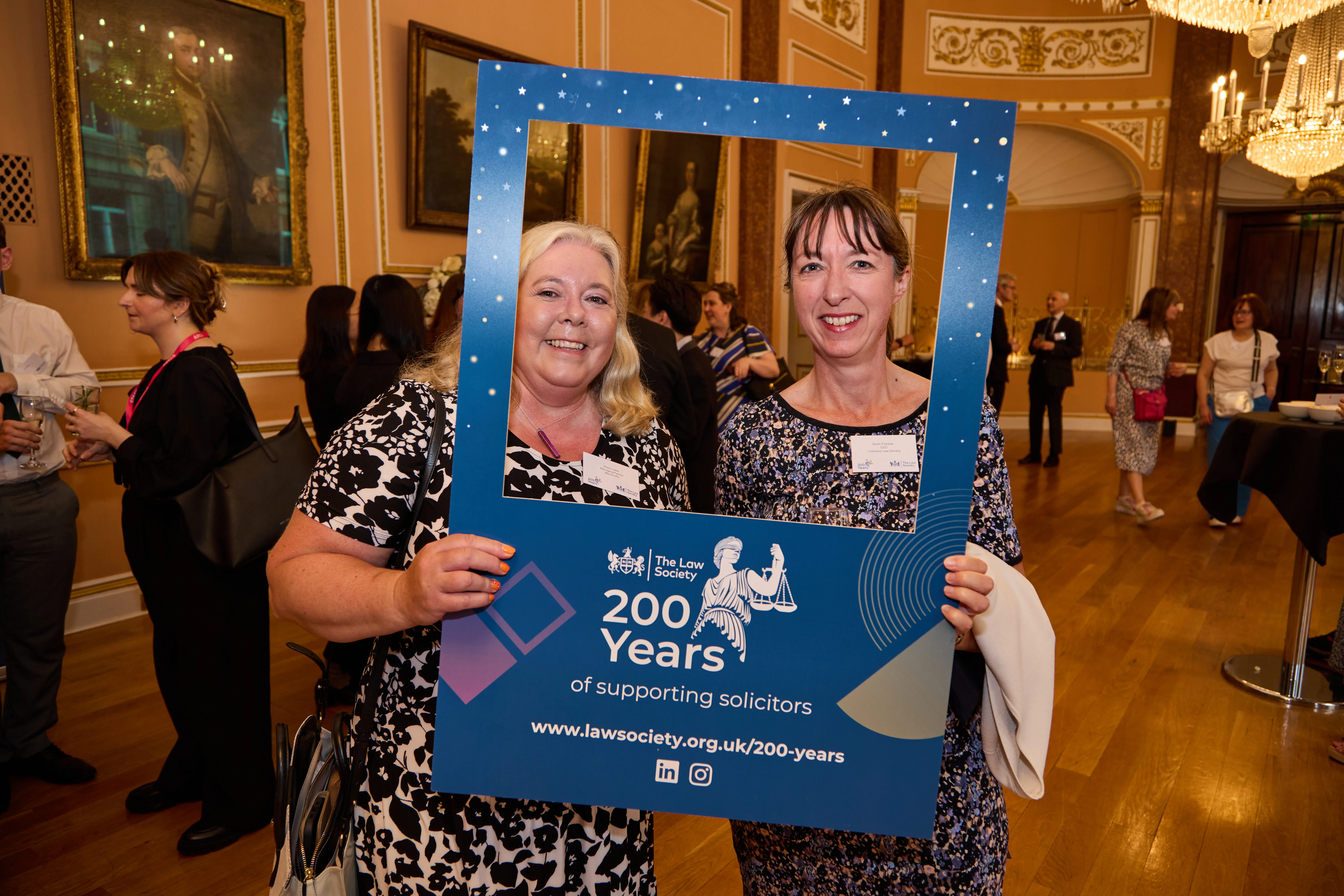 Two women, one blonde, one brunette posing and smiling behind bicentenary photo frame