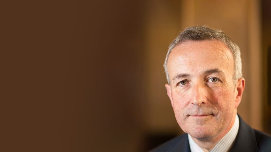 Robert Bourns is a white man with short, dark grey hair. He is smiling and wears a black suit with a white shirt.