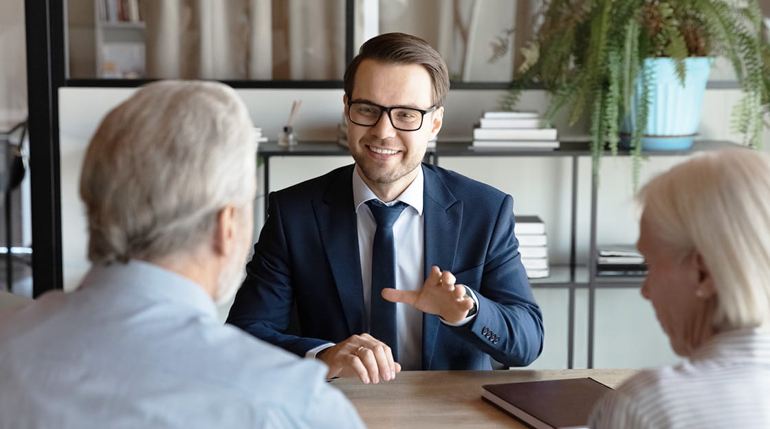 A lawyer sits opposites two older clients and smiles at them.