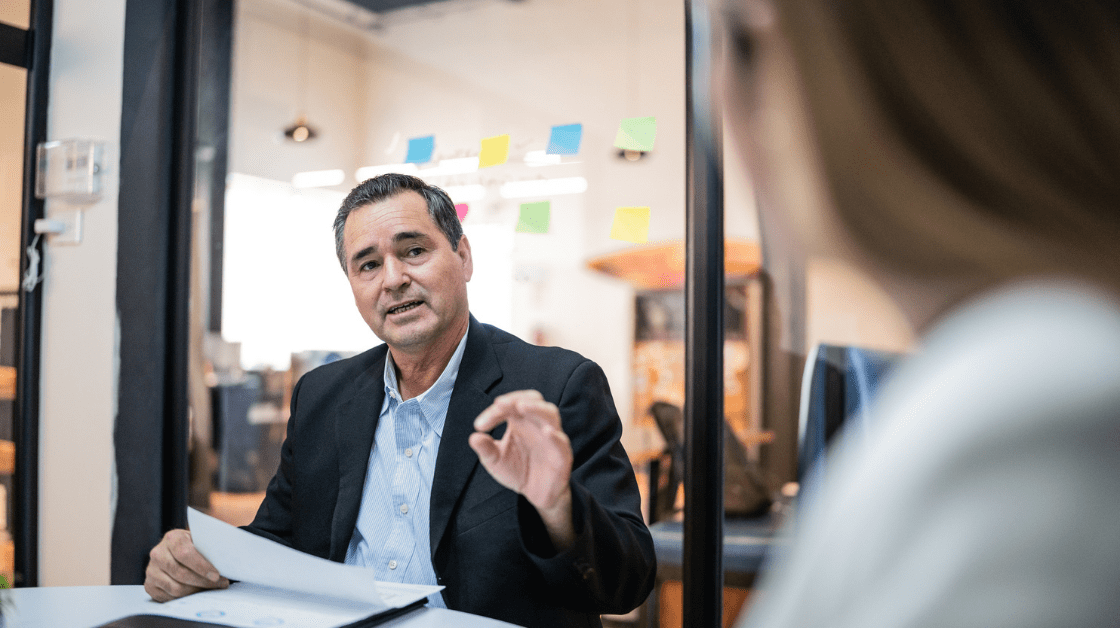 Male consultant sitting in office holding documents talking with female colleague 