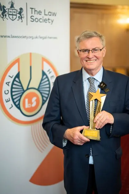 Solicitor Duncan McNair smiles holding his Legal Heroes award at the 2024 event. He is smartly dressed wearing a suit and tie.