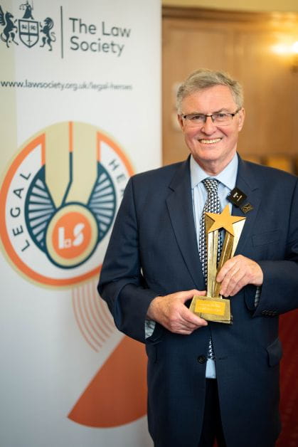 Solicitor Duncan McNair smiles holding his Legal Heroes award at the 2024 event. He is smartly dressed wearing a suit and tie.