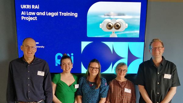 Panel members, two men and three women are standing front of a board which says AI law and legal training project. They are all smiling.