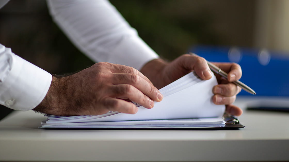 A man's hands leaf through a stack of papers. 