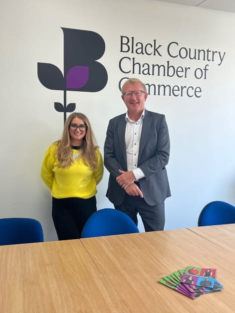 Solicitor Emma Chater stands with a male colleague in front of signage saying "Black Country Chamber of Commerce". They are both smiling and are dressed professionally