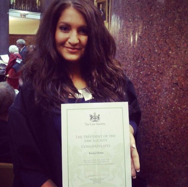 Solicitor Emma Chater smiles while holding her admissions certificate whilst wearing formal dress in the Law Society library