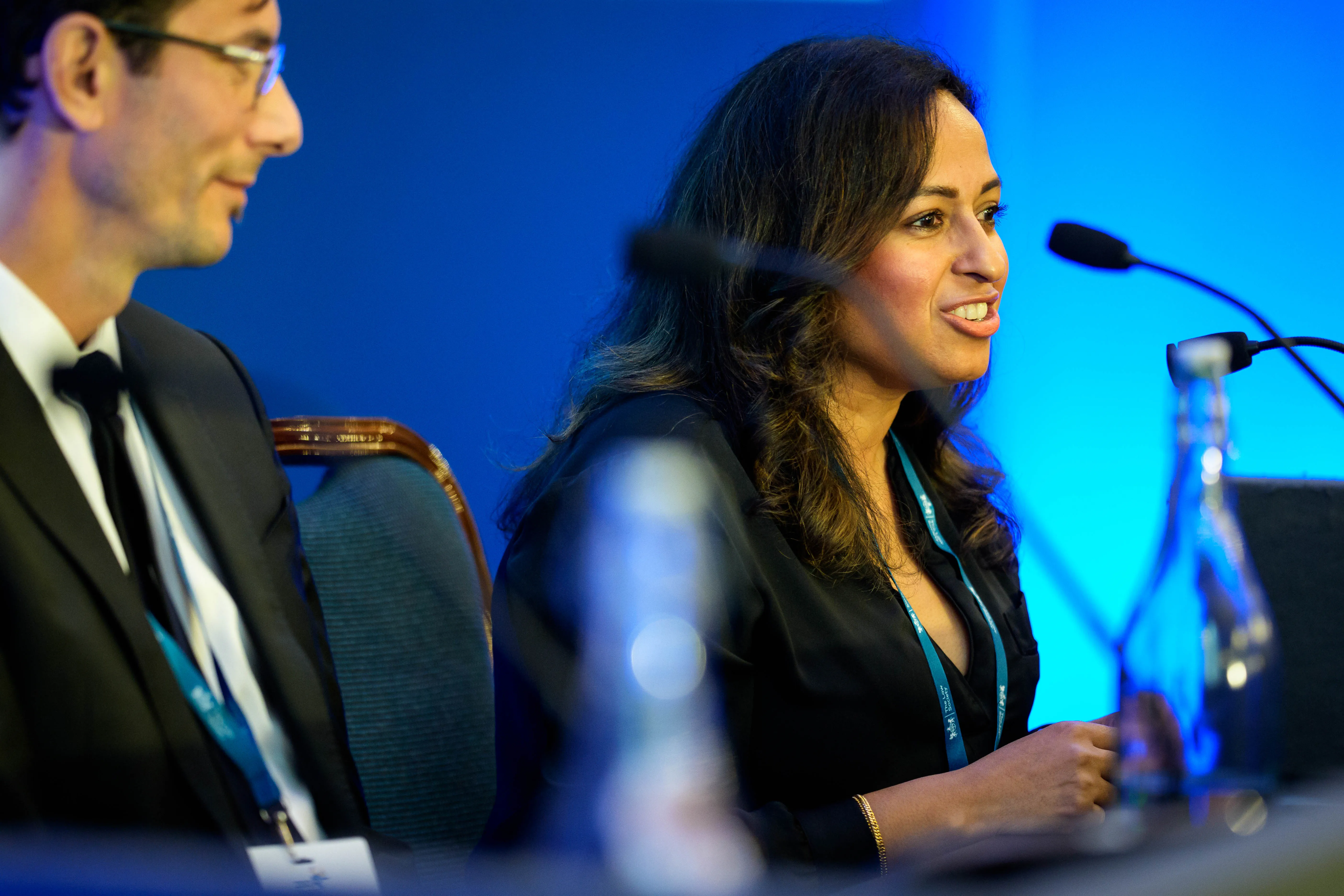 Nisha Morjaria speaks into a microphone as part of a panel, while another panellist listens.