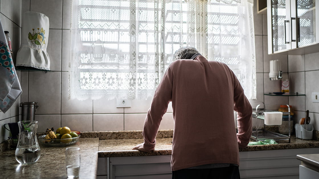 A vulnerable person stands hunched over a kitchen sink with their back turned.